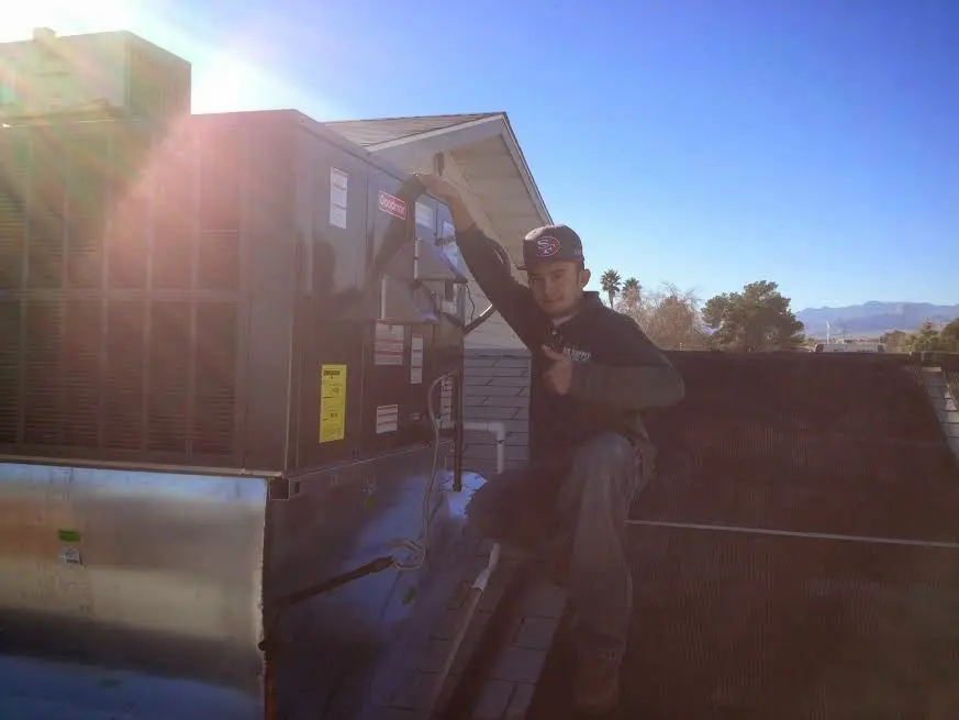 HVAC technician performing Air Duct Repair on a rooftop unit in Orosi